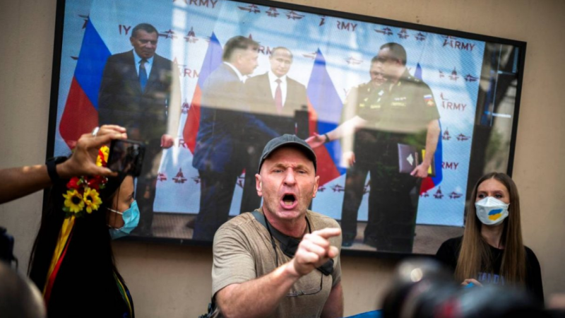 Bangkokā dzīvojošie ukraiņi un viņu atbalstītāji runā pie televizora ekrāna, kurā tiek rādīta Krievijas prezidenta Vladimira Putina video uzruna