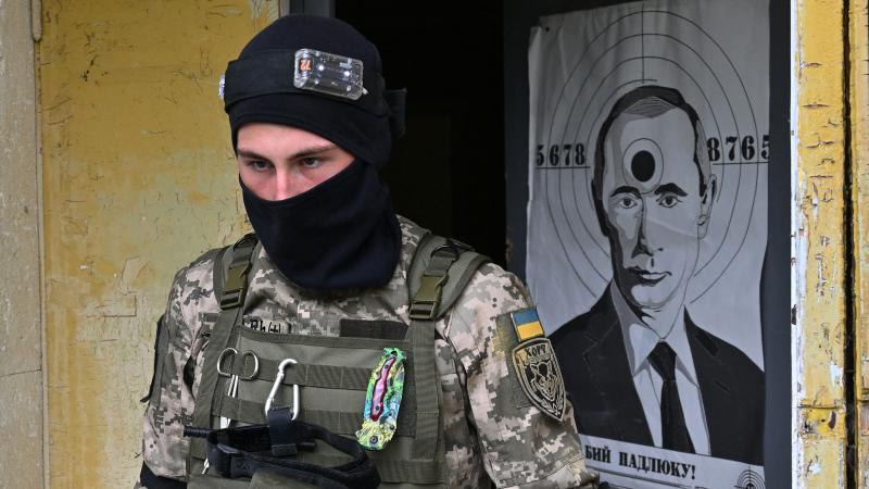 Ukrainas teritoriālās aizsardzības vienības karavīrs pamet ēku, kurā ir plakāts šaušanas mērķa formā ar Putina attēlu