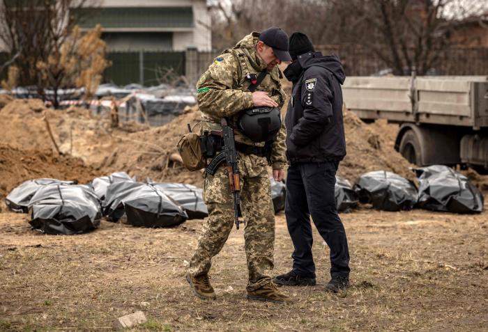 Ukrainas bruņoto spēku karavīrs un policists apsargā krievu okupantu kara noziegumu upuru ekshumāciju Bučā / AFP / Scanpix