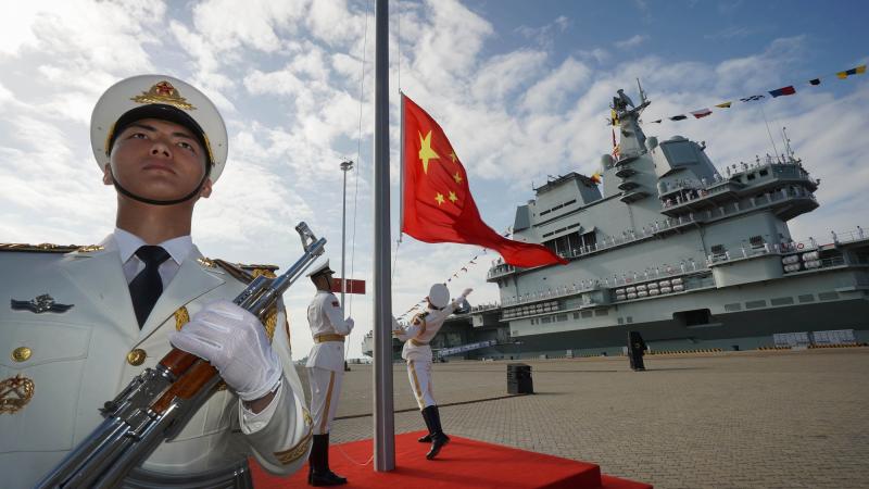 Ķīnas karavīri paceļ karogu, atklājot jauno Tautas atbrīvošanas armijas jūras spēku aviācijas bāzes kuģi