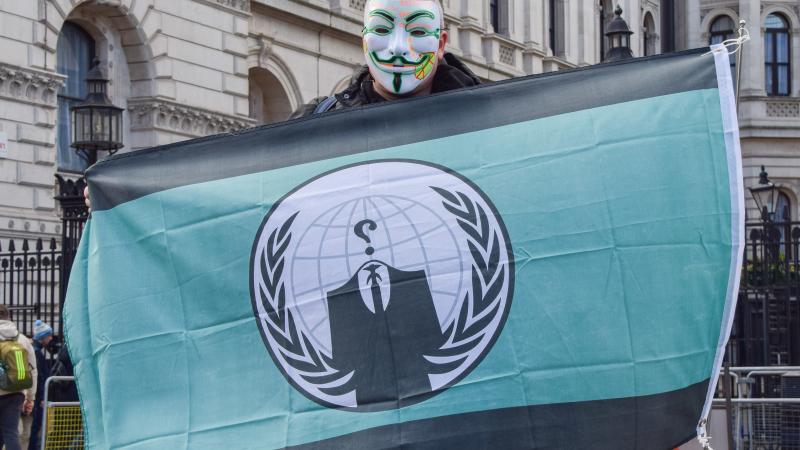 Protestēt\ajs Londonā rokās tur karogu ar "Anonymous" logo