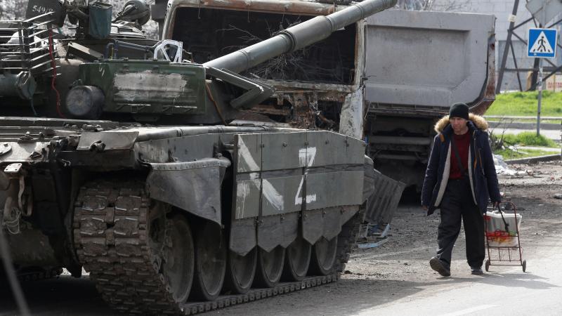 Mariupoles iedzīvotājs iet gar krievu okupantu tanku