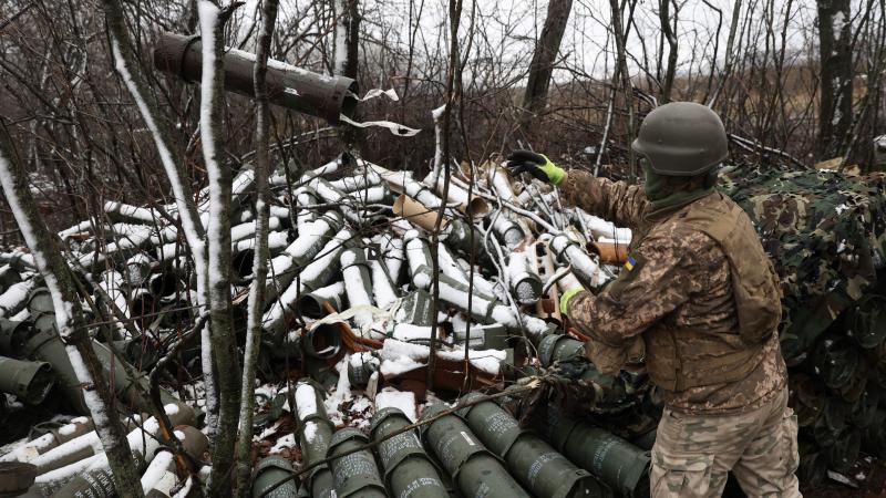 Ukraiņu karavīrs pie izlietoto 155mm artilērijas lādiņu korpusu kaudzes