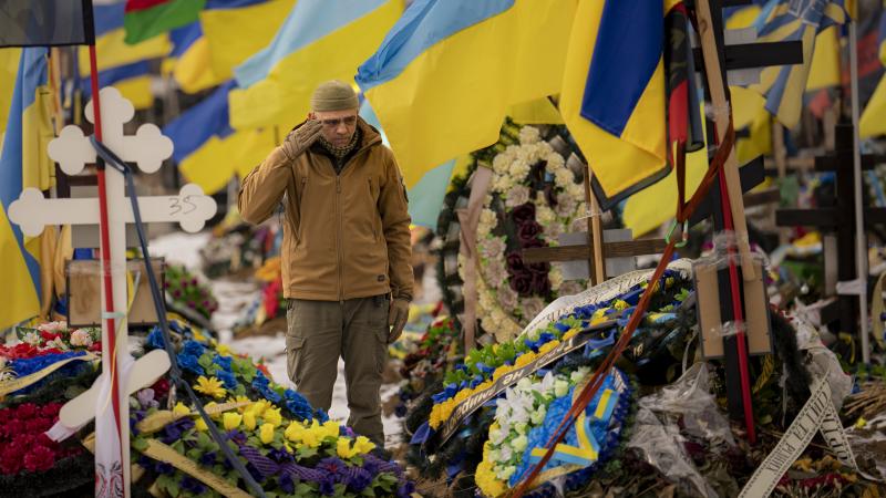 Ukrainas karavīrs salutē saviem kritušajiem biedriem, stāvot karavīru brāļu kapos