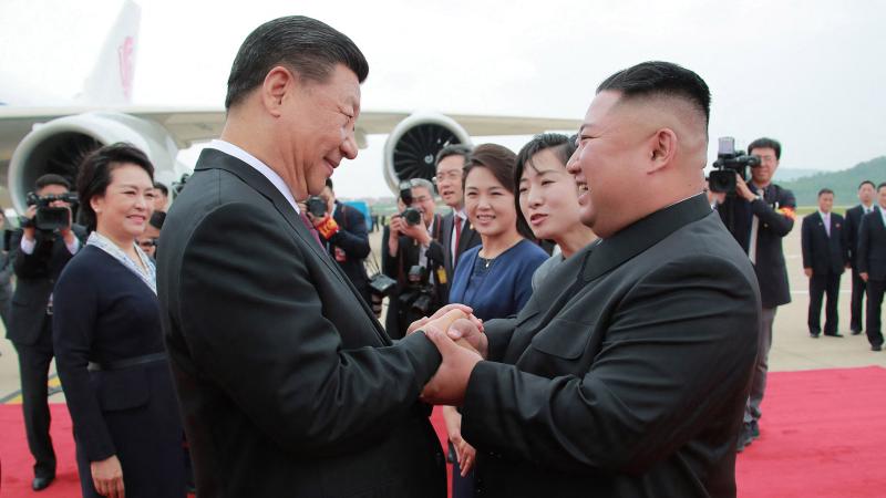 Ķīnas prezidents Sji Dzjiņpins un Ziemeļkorejas līderis Kims Čenuns tur rokas
