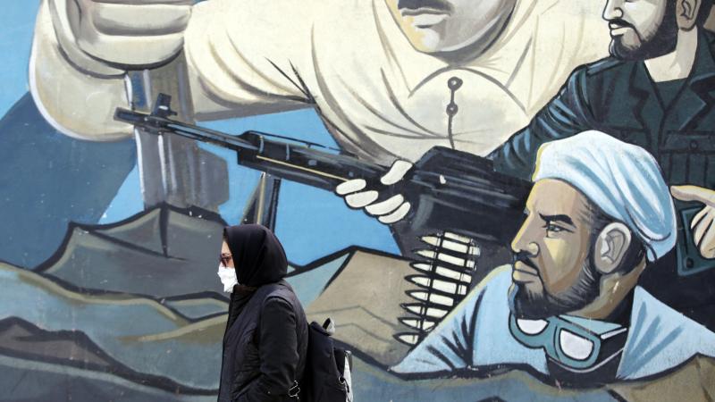 Sieviete iet garām sienas murālim, kur uzzīmēti Irānas revolūcijas kaujinieki